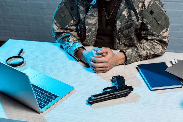 cropped view of military man sitting with clenched hands near gun 