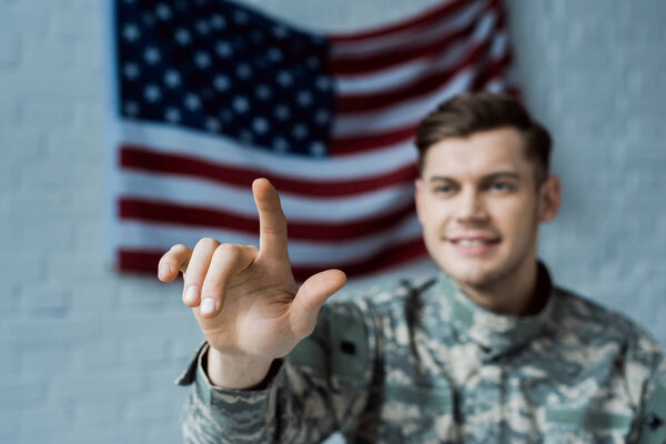 selective focus of happy man in military uniform pointing with finger near american flag