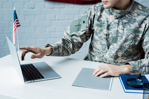 cropped view of soldier pointing with finger at laptop in office 