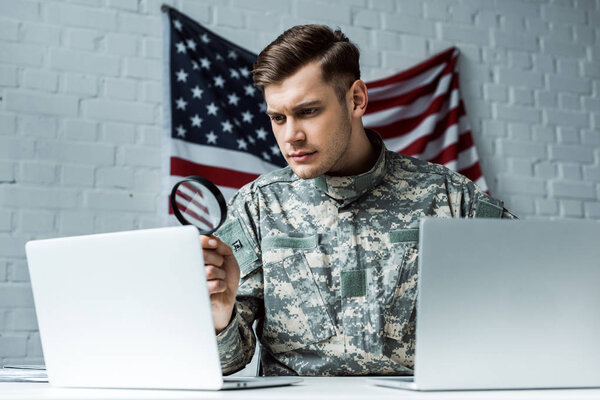 handsome soldier holding magnifying glass near laptops 