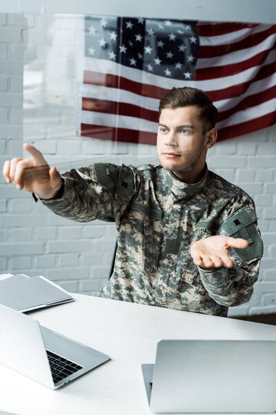handsome soldier in uniform gesturing near laptops in office 