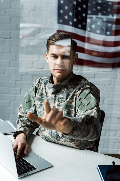 selective focus of handsome man in camouflage uniform pointing with finger in office 