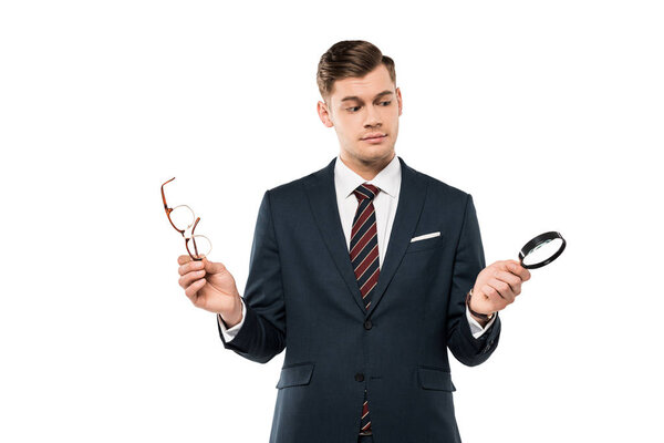 handsome businessman holding glasses and magnifying glass isolated on white 
