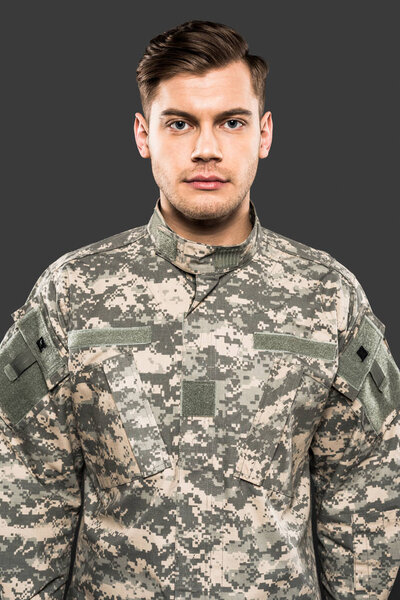 serious soldier in uniform looking at camera isolated on grey