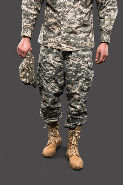 cropped view of soldier holding cap and standing isolated on grey 