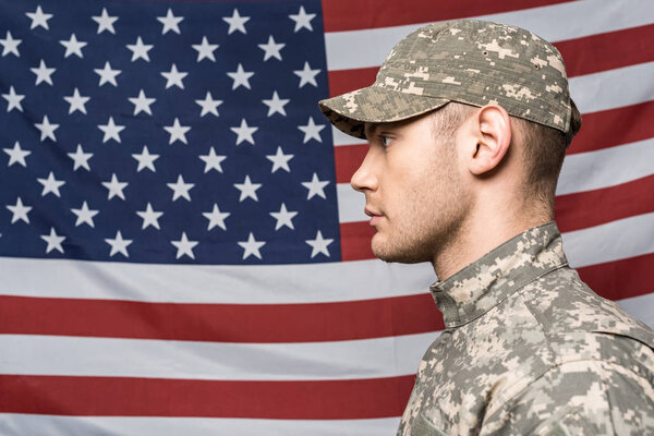 handsome man in military uniform and cap near flag of america