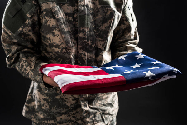 cropped view of man in military uniform holding flag of america isolated on black