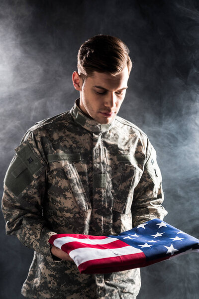 handsome man in military uniform looking at american flag on black with smoke 