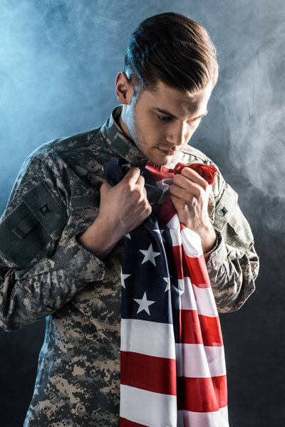 upset soldier holding american flag on black with smoke 