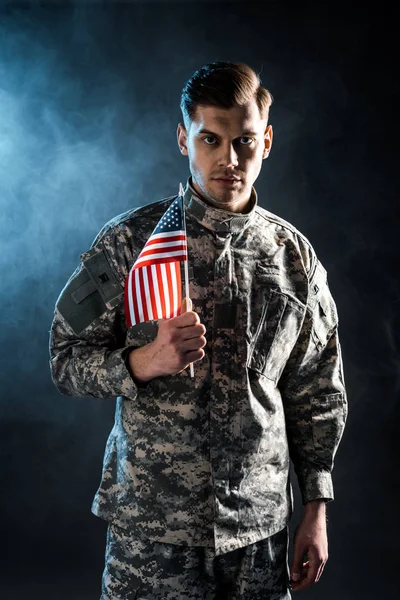 煙で黒い上にアメリカの旗を持っている自信のある兵士 — ストック写真