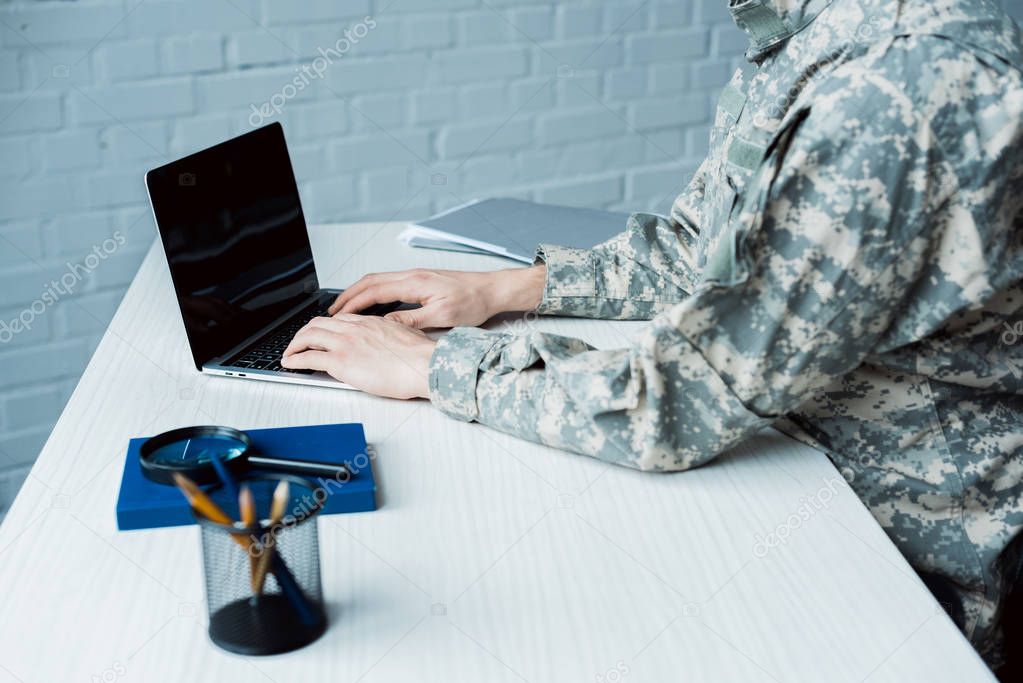 cropped view of military man using laptop with blank screen 
