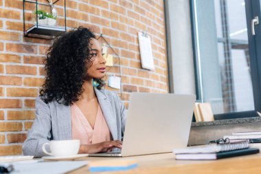 dizüstü bilgisayar ile ofis masasında oturan afro-amerikan Casual iş kadını