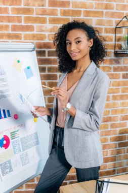 gülümseyen afrikalı amerikalı Casual iş kadını loft ofiste flipchart yakınında poz