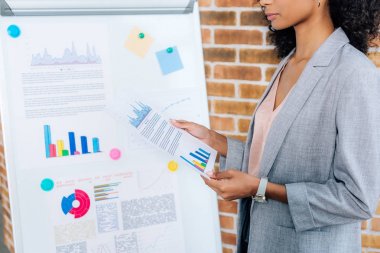 loft ofiste flipchart yakın grafik ile kağıt tutan Afrikalı amerikalı Casual iş kadını kırpılmış görünümü