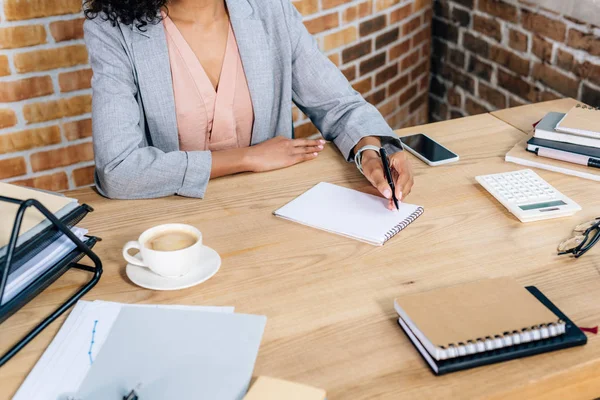loft ofiste masada not defterine yazan Afrikalı-Amerikalı Casual iş kadını kırpılmış görünümü