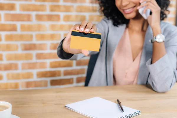 アフリカ系アメリカ人カジュアルビジネスウーマンがクレジットカードを提示し スマートフォンで話す — ストック写真