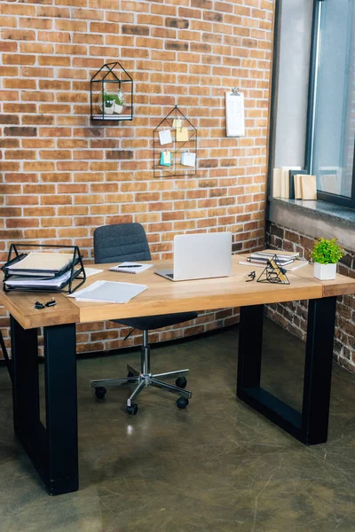 desk with laptop and documents in modern loft office with brick wall