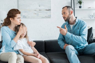 kanepede otururken karısını parmakla işaret eden sakallı adam 