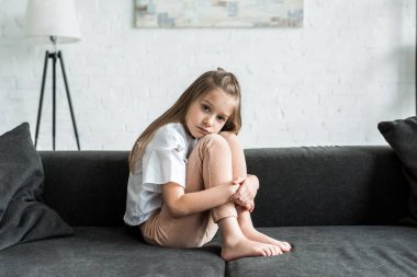 kanepede oturan üzgün çocuk ve evde kamera bakıyor 