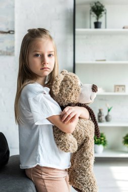 cute kid looking at camera and holding teddy bear at home  clipart