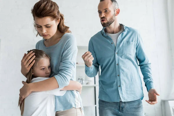 Upset Mother Hugging Daughter While Angry Man Showing Fist Home — Stock Photo, Image