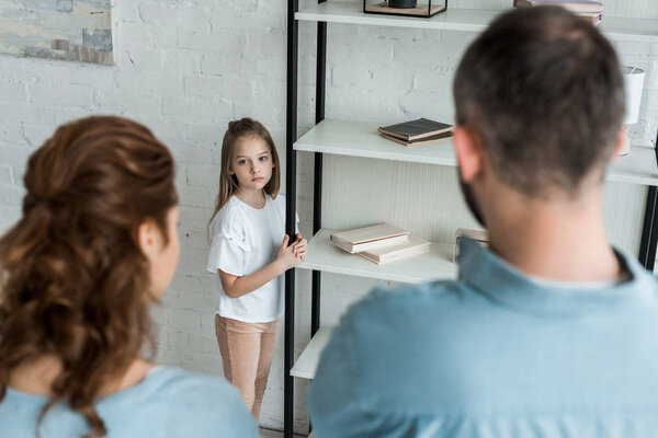 selective focus of upset child looking at parents at home 