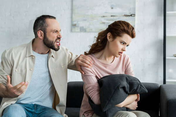 irritated man touching shoulder of offended woman at home 