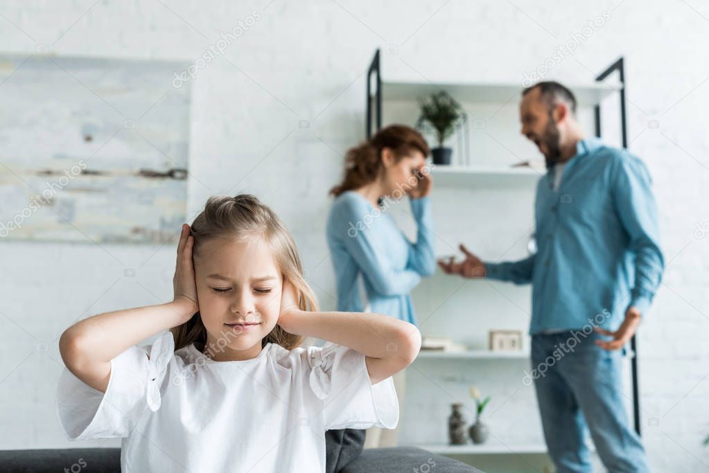 selective focus of kid with closed eyes covering ears near parents at home 