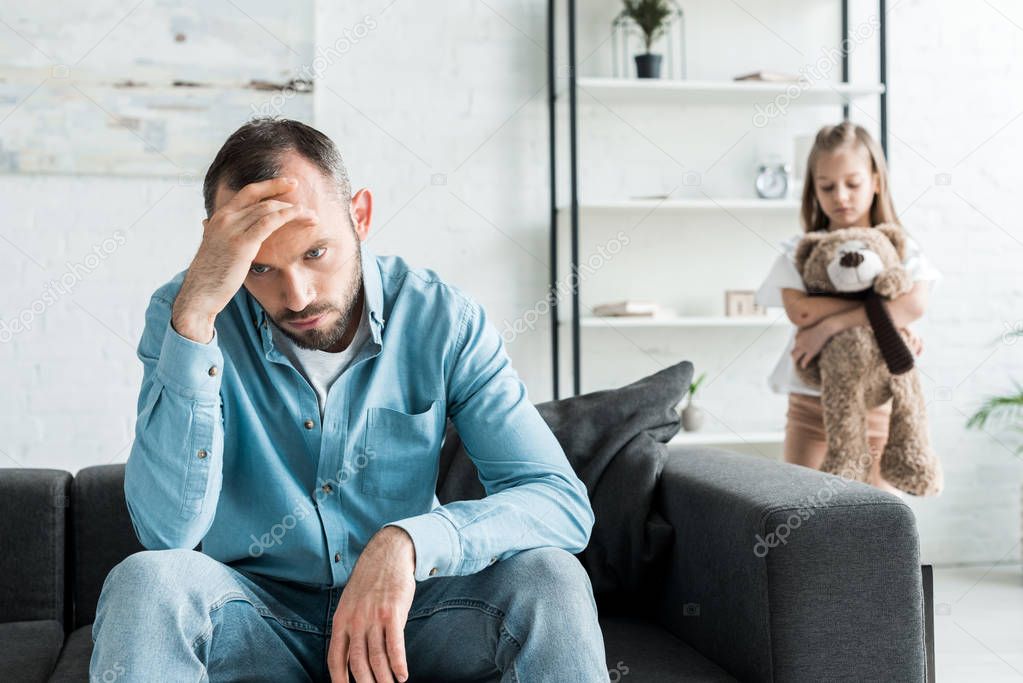 selective focus of upset man sitting on sofa near daughter at home 