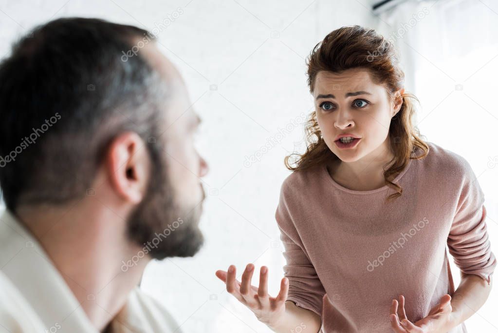 selective focus of offended woman gesturing while looking at man 