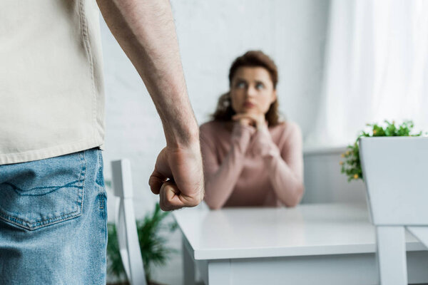 selective focus of angry man threatening with fist while standing near woman 