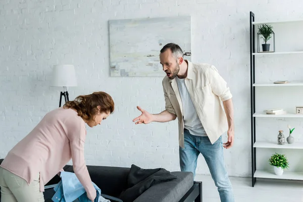 Boze Man Gebaren Terwijl Kijken Naar Vrouw Verpakking Kleren Thuis — Stockfoto