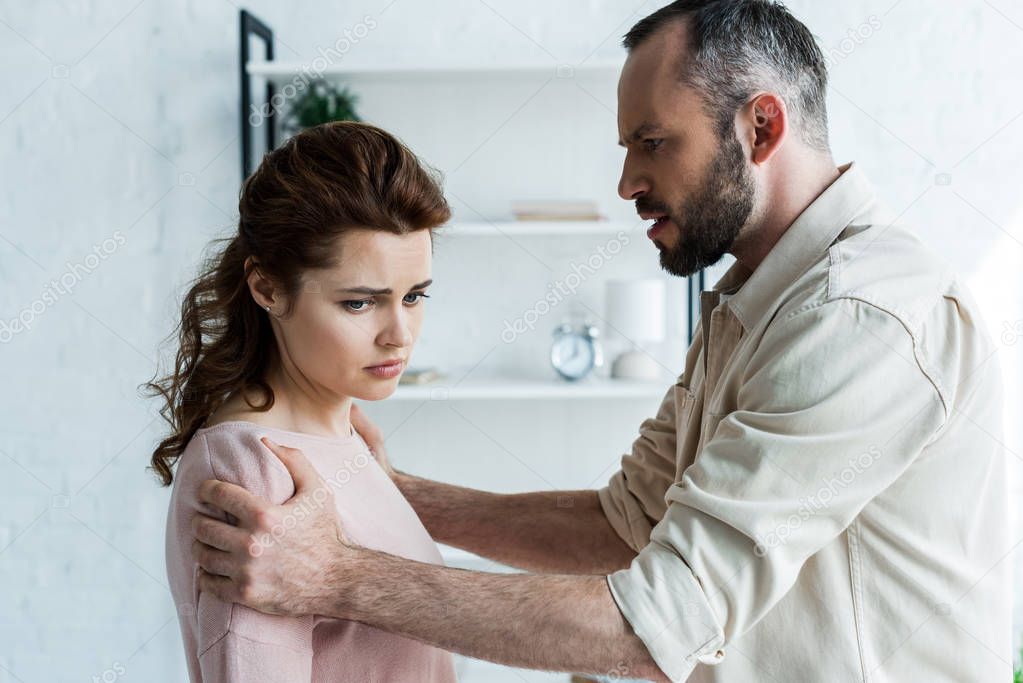 angry man touching offended brunette woman at home 