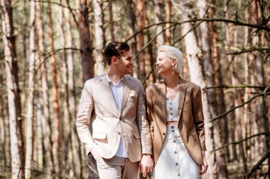 Ormanda yürüyen ve el ele tutuşan gülümseyen çiftin ön görünümü