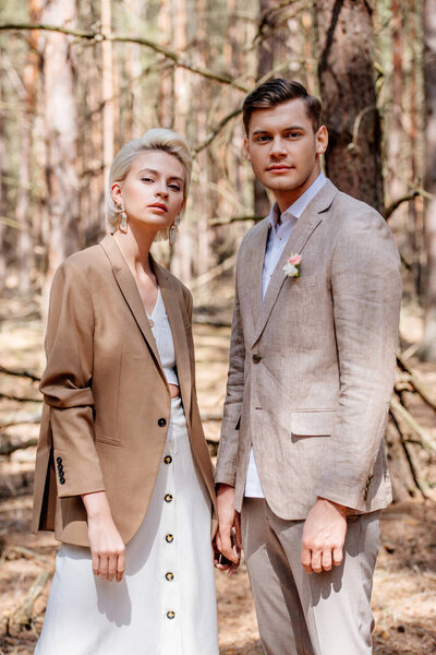 Stylish bride and bridegroom in beige clothing posing in forest
