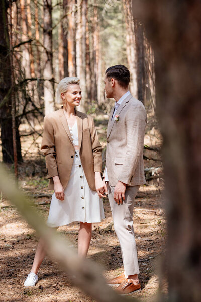 Selective focus of handsome man and attractive woman holding hands in forest