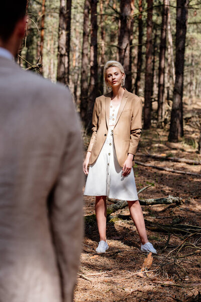 Selective focus of attractive sylish bride looking at bridegroom in forest