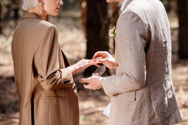 Partial view of man putting on wedding ring on woman finger in forest