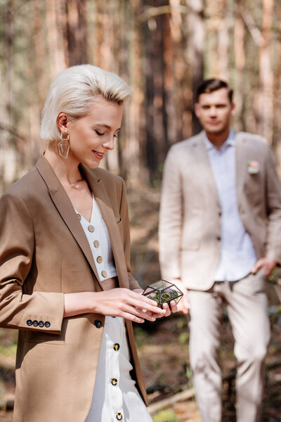 Selective focus of happy woman holding wedding ring and man looking at his woman in forest