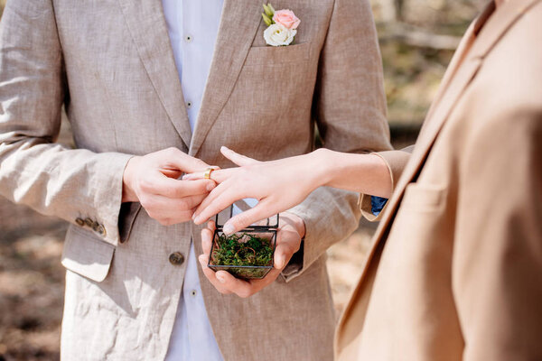 cropped view of bridegroom and bride putting wedding ring on finger
