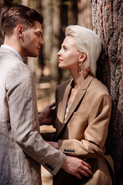 stylish couple in formal wear looking at each other in forest clipart