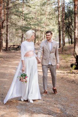 sadece evli çift el ele tutuşarak ve ormanda birbirlerine bakarak gülümseyen tam uzunlukta görünümü