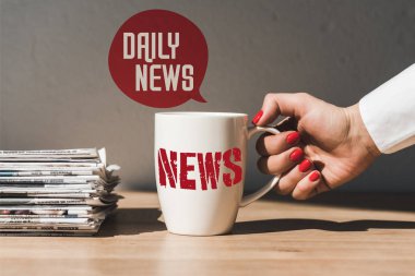 cropped view of woman holding white cup with news lettering on wooden table near pile of different newspapers and speech bubble illustration with daily news text clipart