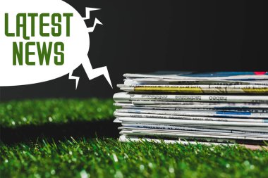 stack of different print newspapers on fresh green grass near speech bubble with green latest news lettering isolated on black clipart