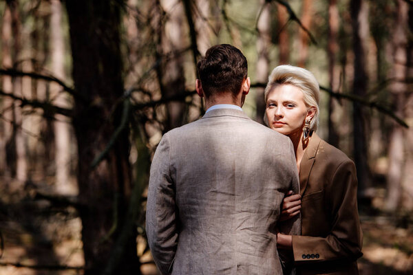 stylish couple in formal wear standing in forest