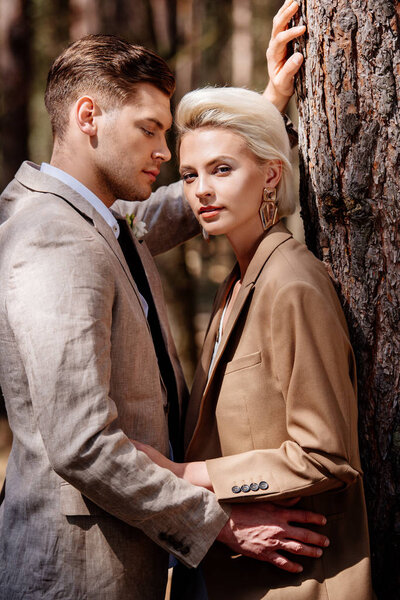 stylish couple in elegant jackets embracing in forest