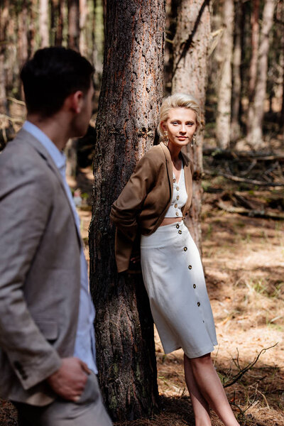 stylish bride and bridegroom standing in forest and looking at each other