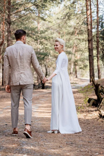 Vista Completa Sonriente Pareja Recién Casados Tomados Mano Caminando Bosque —  Fotos de Stock