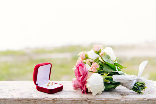 wedding ring in red box and bouquet on wooden surface