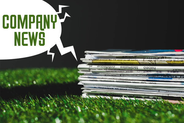 stack of different print newspapers on fresh green grass near speech bubble with company news lettering isolated on black